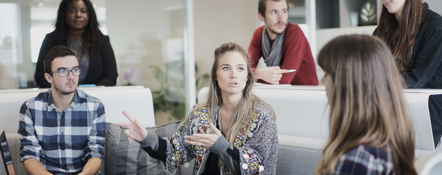 Grupo de personas, algunas de pie y otras sentadas en un sofá, manteniendo una conversación sobre marketing digital